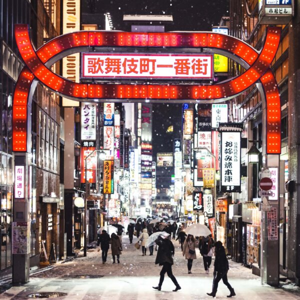 People crossing a snowy road with bright shops around
