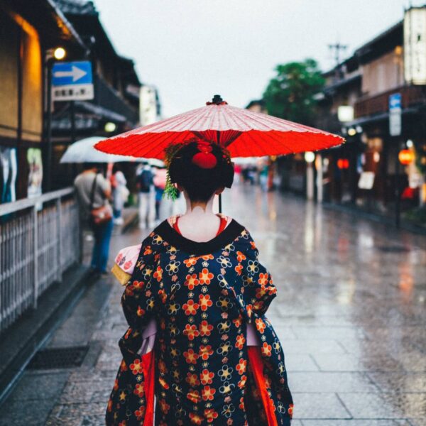 Woman in traditional Japanese kimono holding a red paper umbrella seen from behind