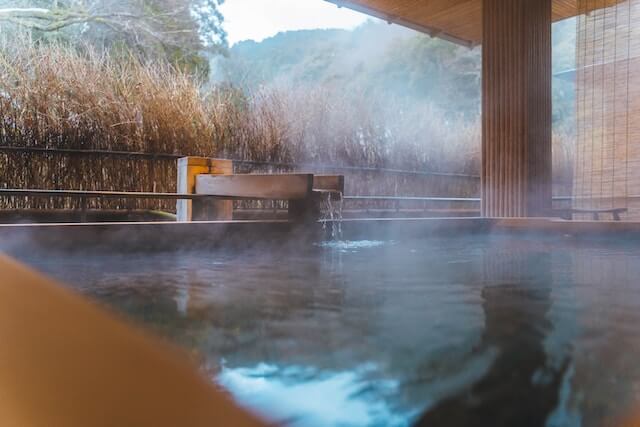 kinosaki hot spring water flowing from wooden spout into bath with mountains in background