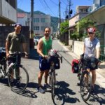 Three men standing next to bikes with big saddlebags in the back on a sunny day in Japan